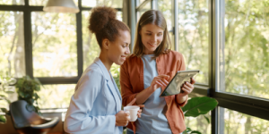 two young woman having coffee on tablet in office