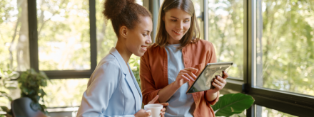 two young woman having coffee on tablet in office