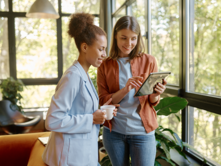 two young woman having coffee on tablet in office