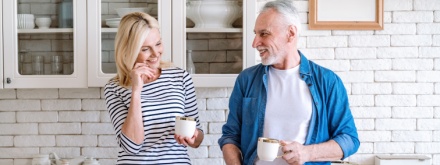Mature woman and man spending time together standing at home kitchen drink tea