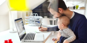 father at home office working with child on his lap 