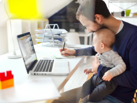father at home office working with child on his lap