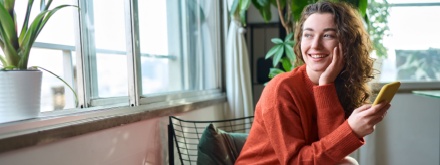 Happy young woman sitting on chair holding mobile phone