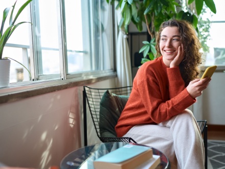 Happy young woman sitting on chair holding mobile phone
