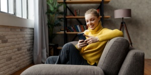 Cheerful young woman using mobile phone while sitting on a sofa at home