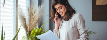 woman on phone reading paper sheet in office with plants