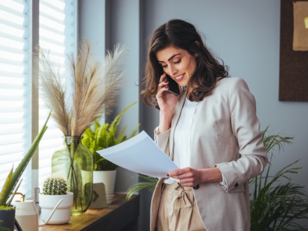 woman on phone reading paper sheet in office with plants