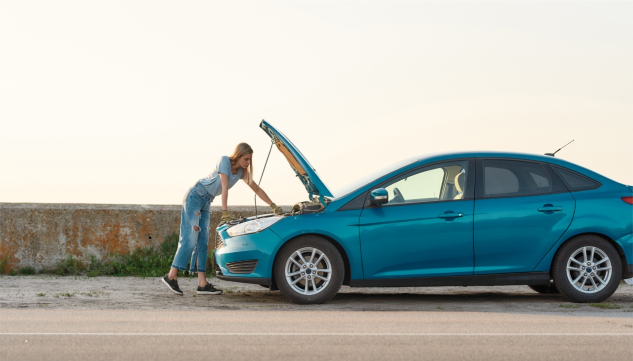 young woman looking under the hood of her broken car