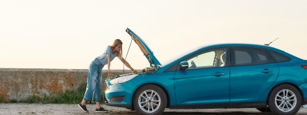 young woman looking under the hood of her broken car