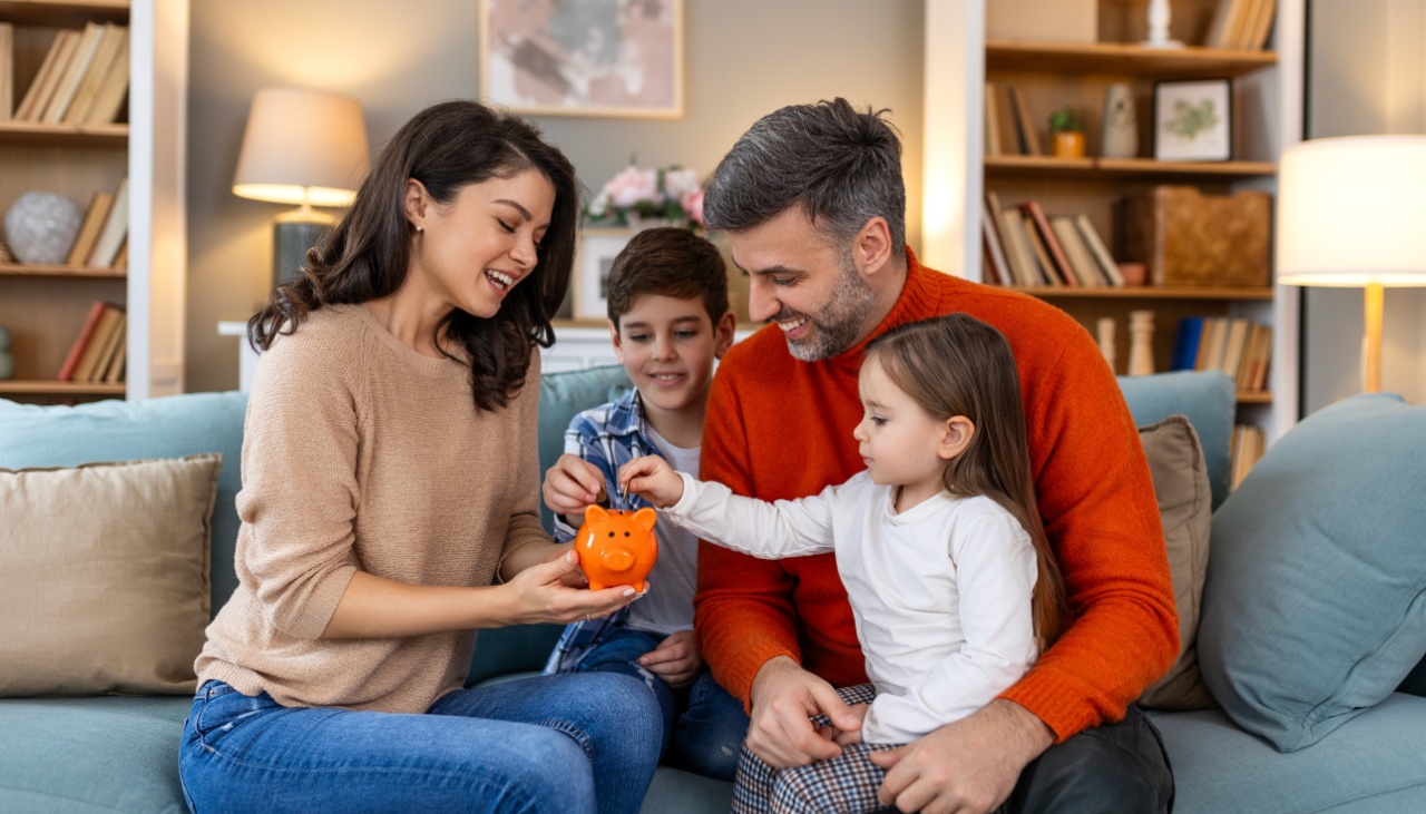 happy family father mother and two children with orange piggy bank