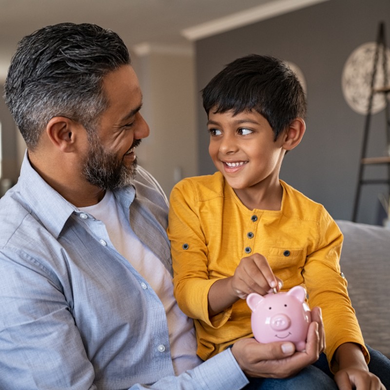 father and boy putting money in piggy bank