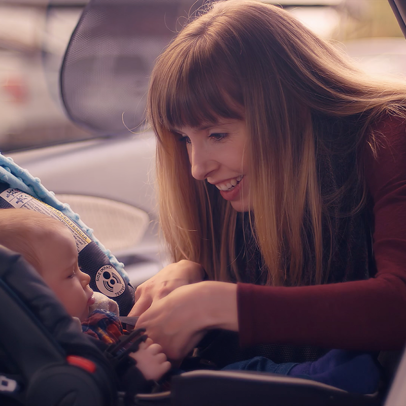 Young mum placing baby into car seat at rear of car