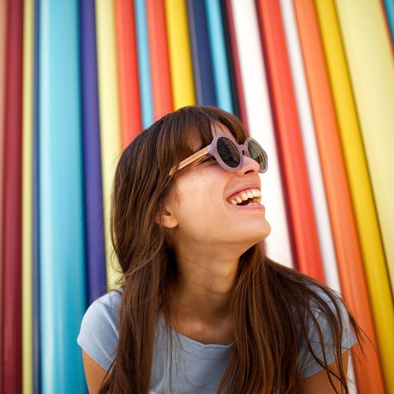 Photo of girl in sun glasses smiling against multi-colour background