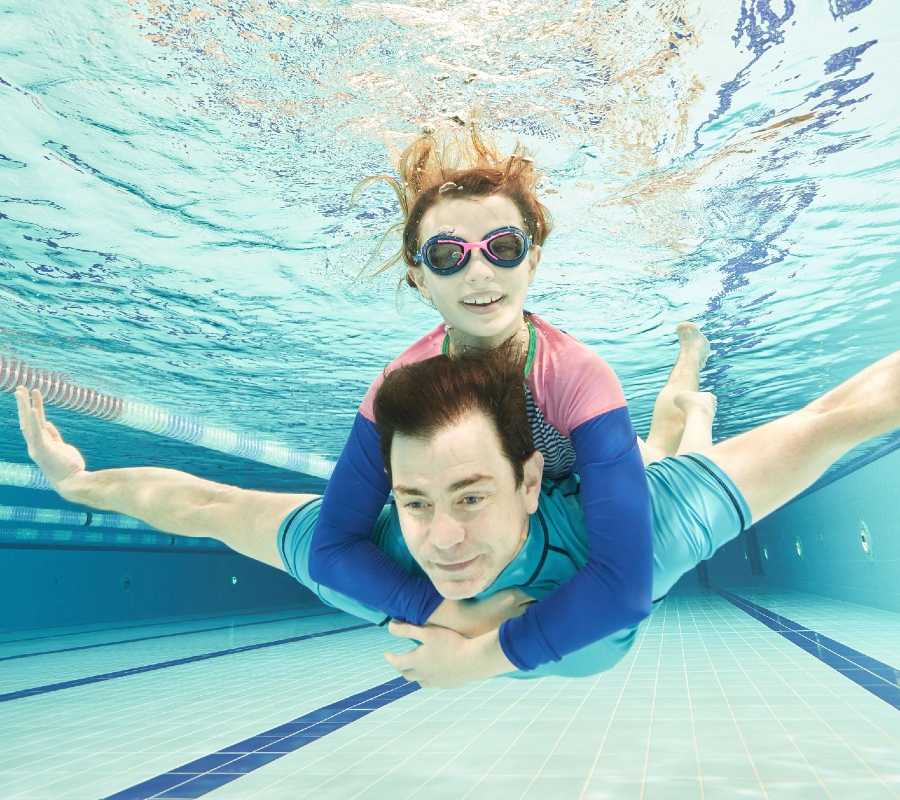 Father and daughter swimming underwater in swimming pool