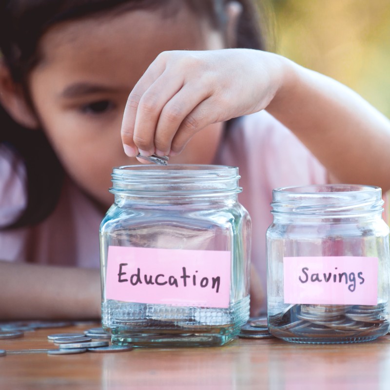 Little girl putting coins into labelled jam jars